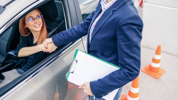 Junge Frau mit Brille sitzt in einem Auto und schüttelt die Hand eines Mannes durch das geöffnete Fahrerfenster
