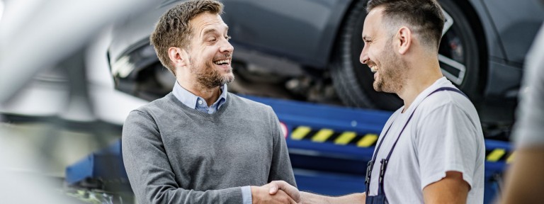 2 Männer geben sich im Autohaus lachend die Hand